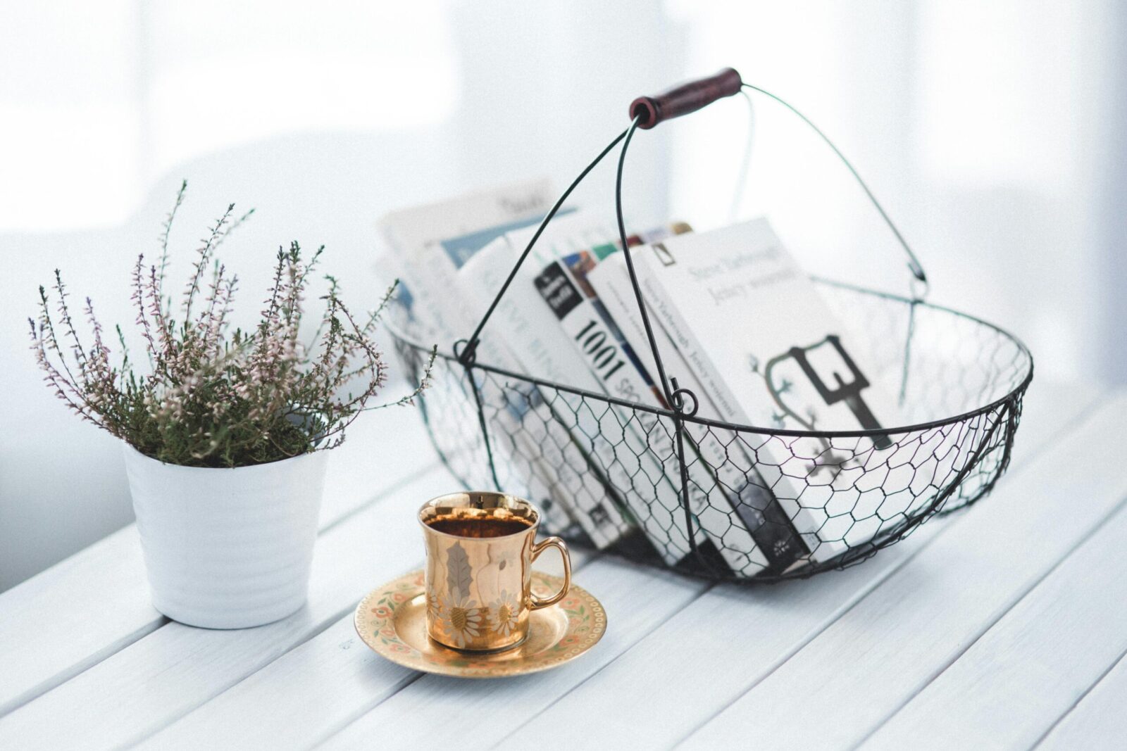 A tranquil home scene featuring a wire basket of books, a golden cup of coffee, and a potted plant on a wooden table.