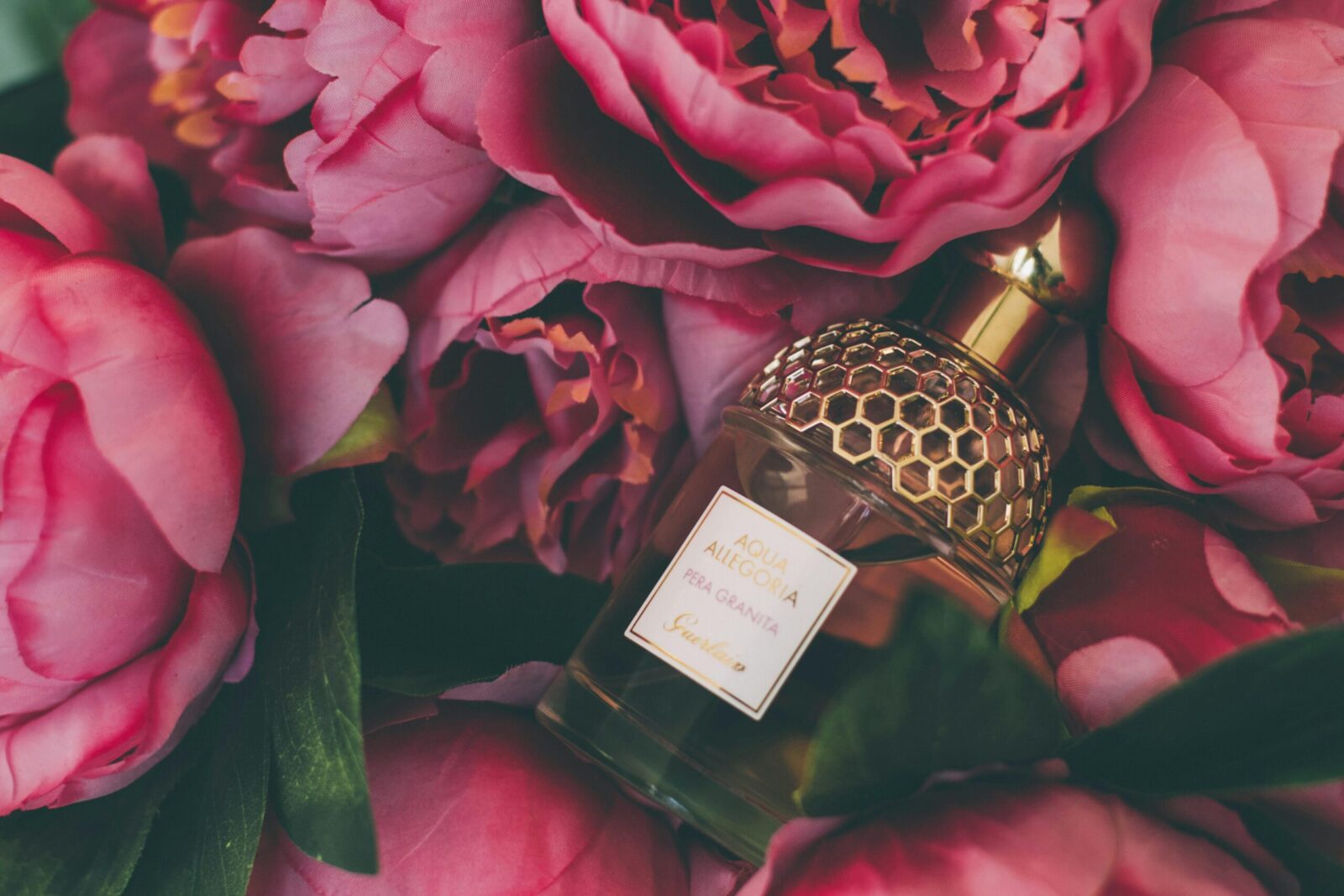 Luxurious perfume bottle nestled within vibrant pink peonies, showcasing elegance and beauty.
